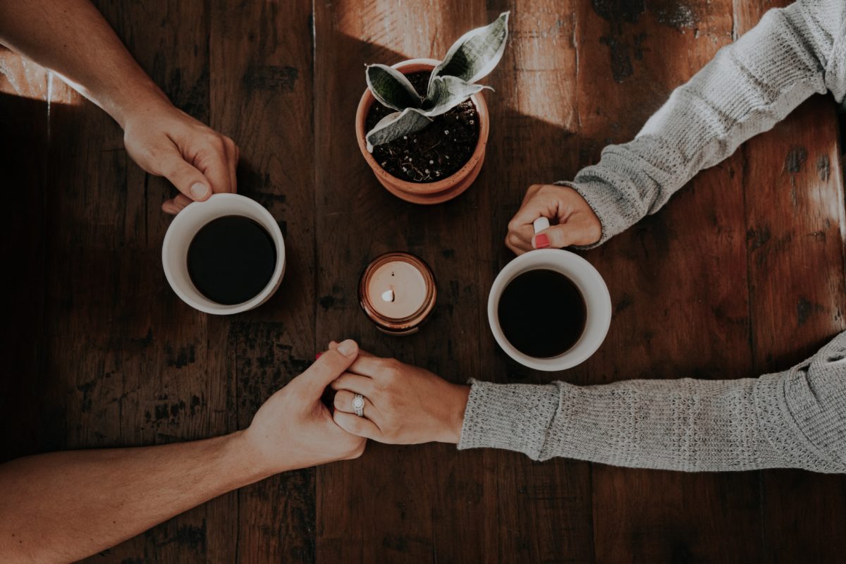 Photo of two people holding hands and white ceramic mugs